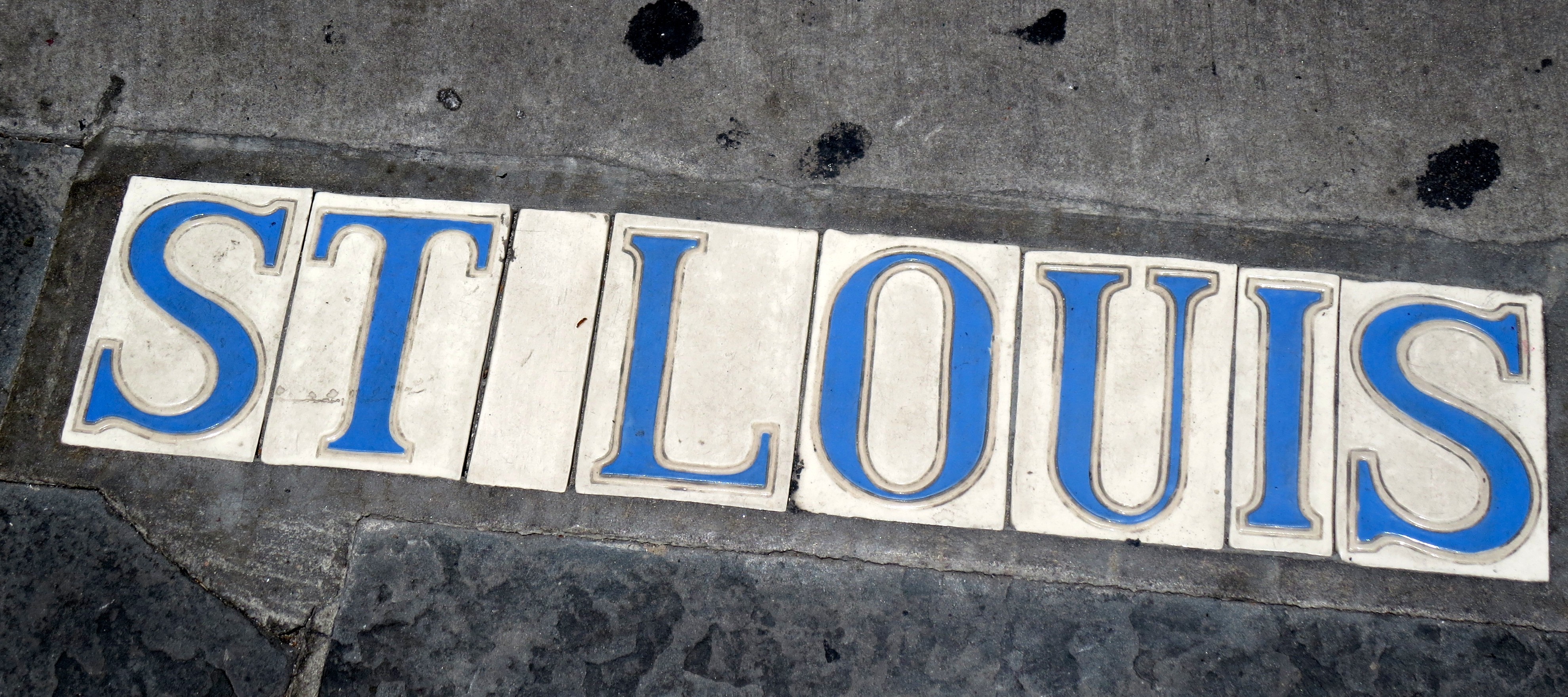 white street tiles with blue lettering spelling St. Louisrivate St. Louis neighborhoods street tiles